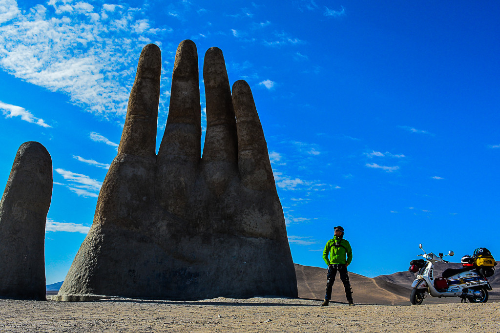 John Silva stands between his fully loaded Vespa (right) and a huge hand sculpture made of stone(left).