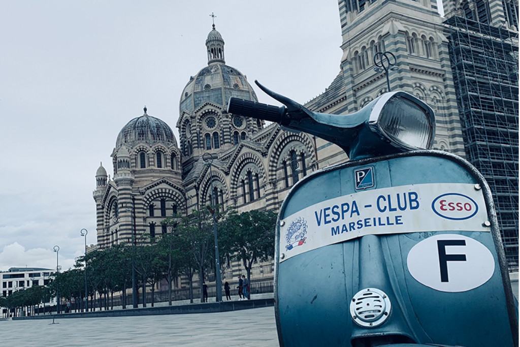 Hellblaue Vespa mit Aufschrift "Vespa Club Marseille" steht vor einem historischen Gebäude