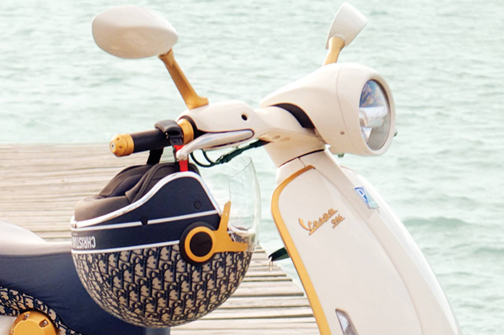 Weiße Vespa mit goldenen Details und Helm im Dior-Design am Lenker. Im Hintergrund ist Wasser Details