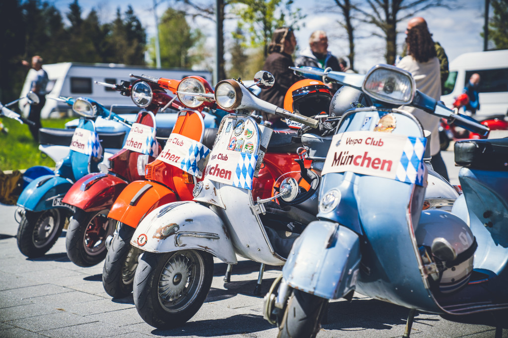 Several Vespas of the Vespa Club Munich are lined up in a car park.