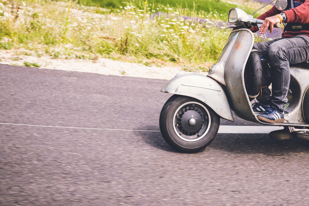 Ausschnitt eines Vespafahrers auf einer Straße im Grünen