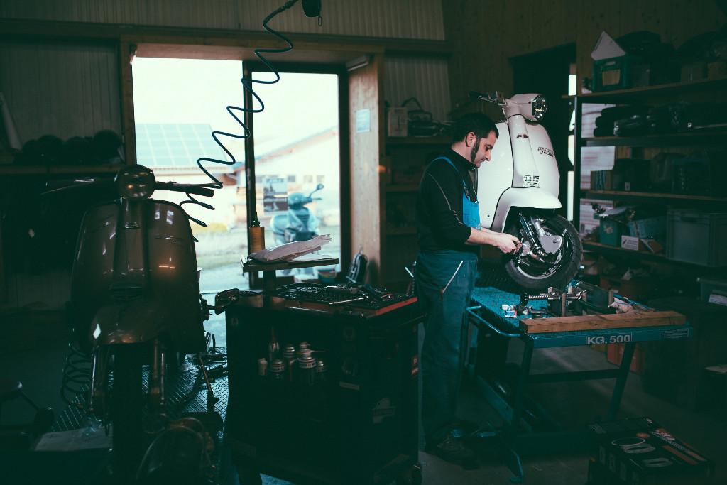 Ein Mann arbeitet an einer Vespa in einer dunklen Werkstatt.