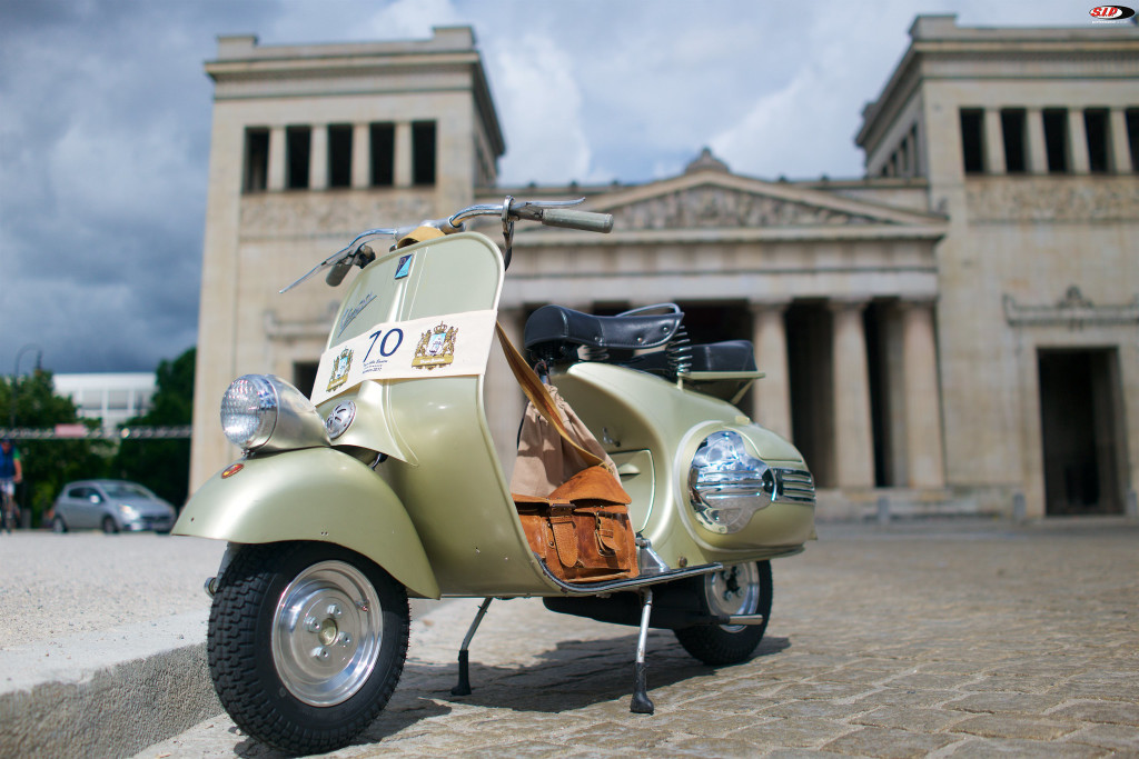 Vespa Wideframe mit einer braunen Tasche steht vor einem alten Gebäude.