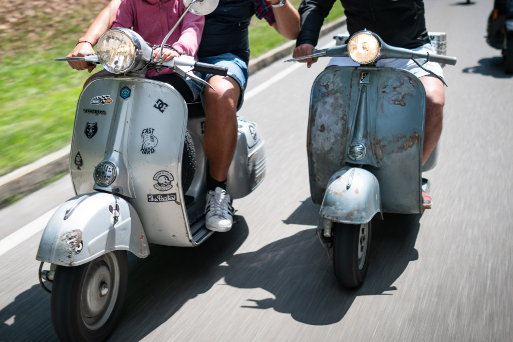 Front view of two moving Vespas on a road.
