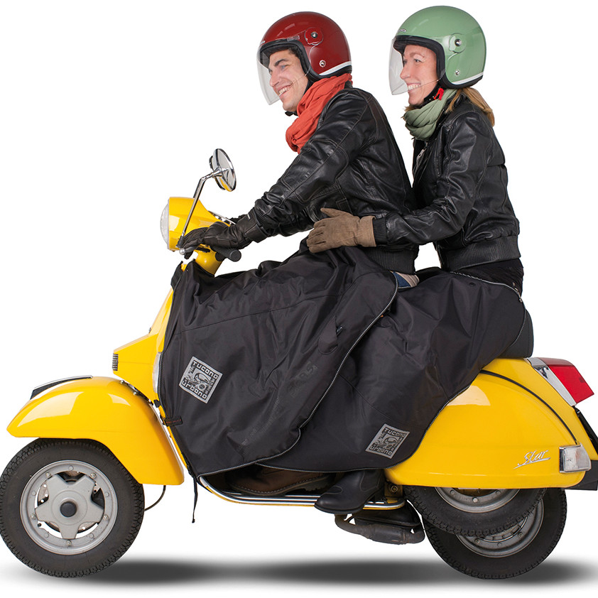 Zwei Personen sitzen auf einer gelben Vespa mit Beinschutz für zwei