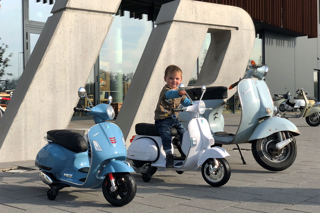 kind sitzt auf kleiner Vespa zwischen einer kleinen und großen Vespa