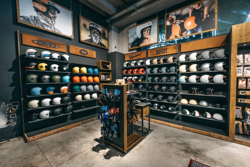 Shelves with scooter helmets and other Vespa accessories, large pictures on the wall above them
