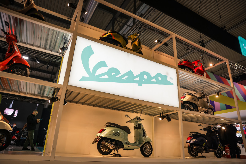 großes Gerüst mit ausgestellten Vespas und einem großen, türkisen Vespa Leuchtschriftzug in der Mitte