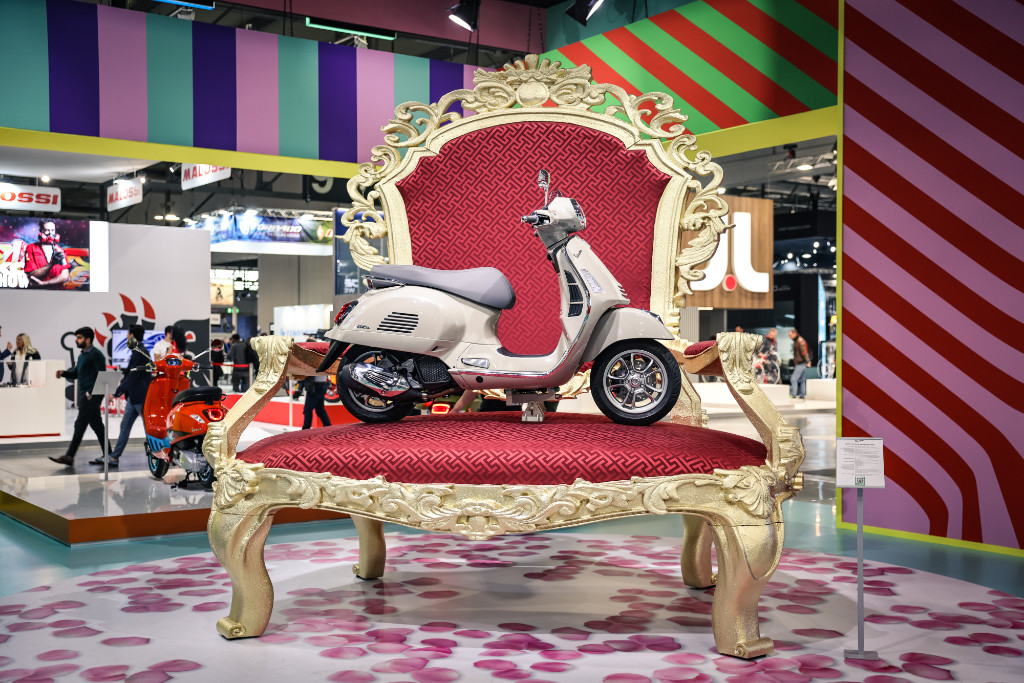 Vespa GTS auf einem riesigen goldenen Thron mit rotem Polster auf der EICMA 22